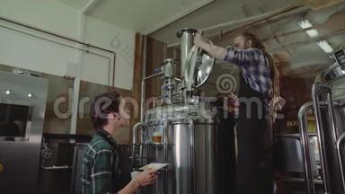 在啤酒厂或啤酒厂工作的有剪贴板的妇女。 啤酒厂工人打开一个啤酒桶的盖子在一个工艺啤酒